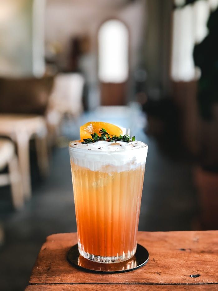 Transparent crystal glass of orange cocktail with white foam and fruit on top